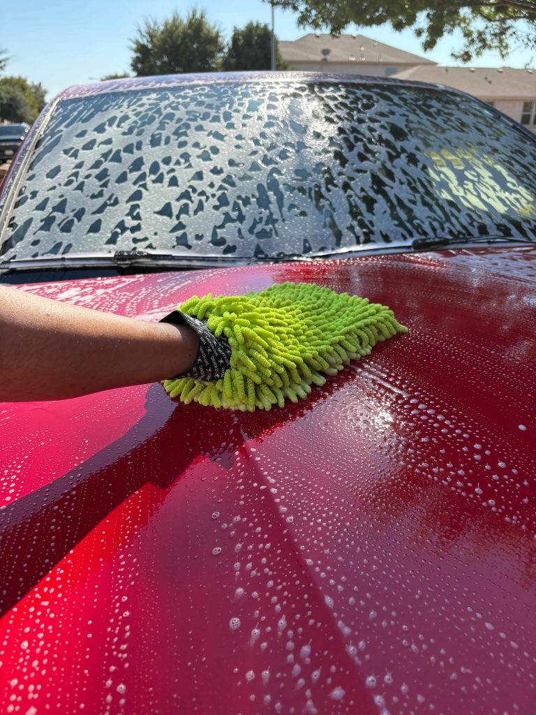 Hand washing a red vehicle with microfiber mitt during mobile exterior detailing by Luna Car Wash & Detailing in DFW